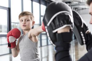 Ein Kind schlägt mit Boxhandschuhen in die Pratzen von seinem Trainer