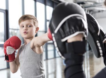 Ein Kind schlägt mit Boxhandschuhen in die Pratzen von seinem Trainer