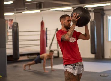 Zwei Personen beim HIIT Training. Eine Person wirft einen schweren Ball, die andere Person macht Liegestütz