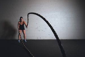 Eine Frau beim High Intensity Intervall Training mit zwei 'Battle Ropes' die sie schwingt.